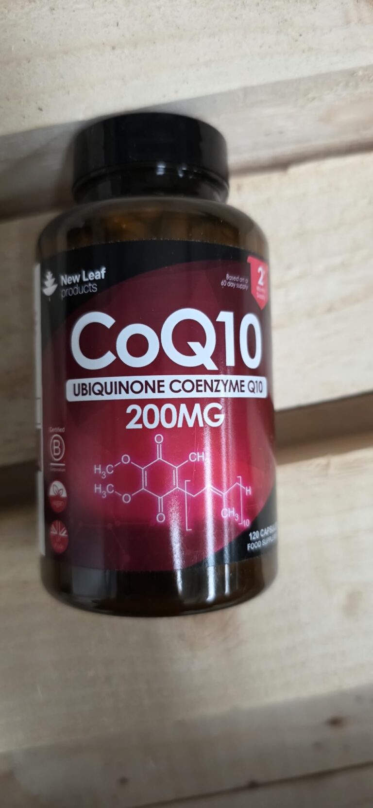 Bouteille de compléments alimentaires CoQ10 sur une surface en bois, vue du dessus et de côté.