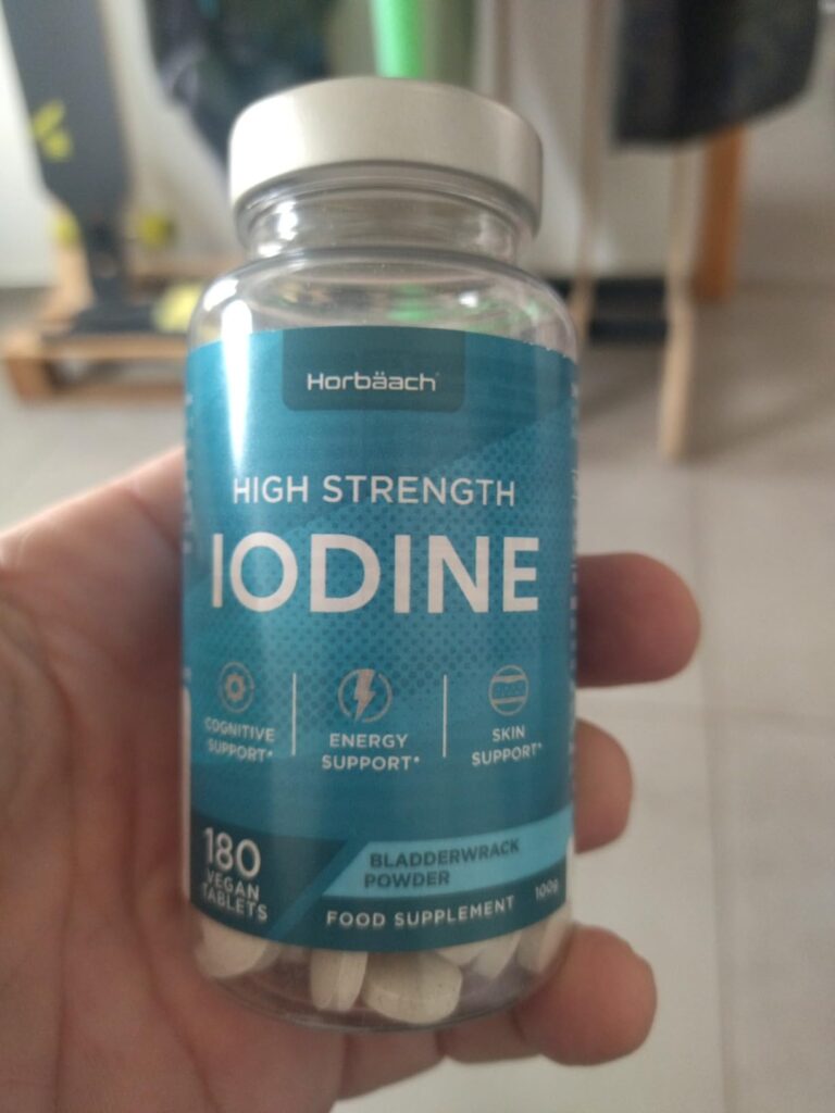 Flacon de compléments alimentaires à l'iode, vu de face, tenu à la main