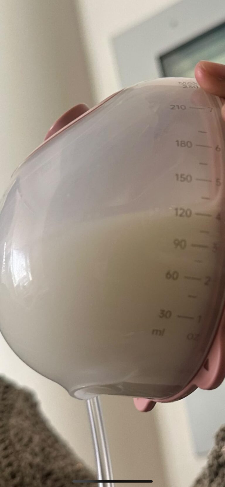 Gros plan sur un biberon avec du lait maternel et un tuyau de tire-lait. Le biberon a des graduations.