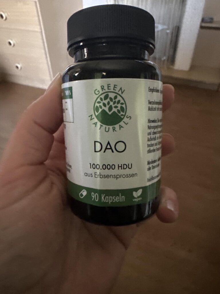 Flacon de capsules DAO dans une main, avec un arrière-plan flou d'intérieur.