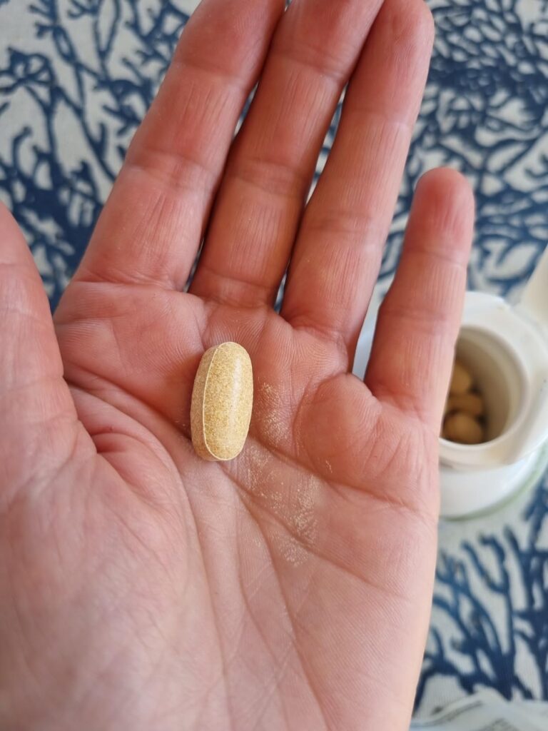 Une pilule de chardon-marie est tenue dans la paume d'une main, avec un flacon blanc partiellement visible en arrière-plan. L...