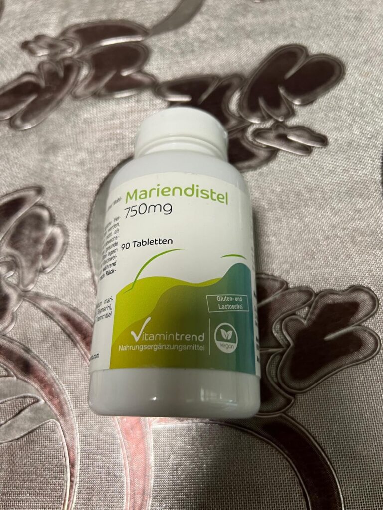 Un flacon blanc de Mariendistel (chardon-marie) est posé sur une surface texturée. L'étiquette du flacon est visible et indiq...