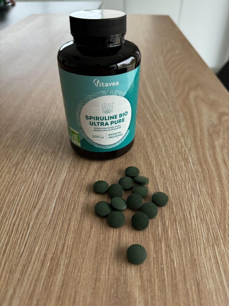 Bouteille de spiruline Vitavea avec des comprimés verts étalés sur une table en bois.