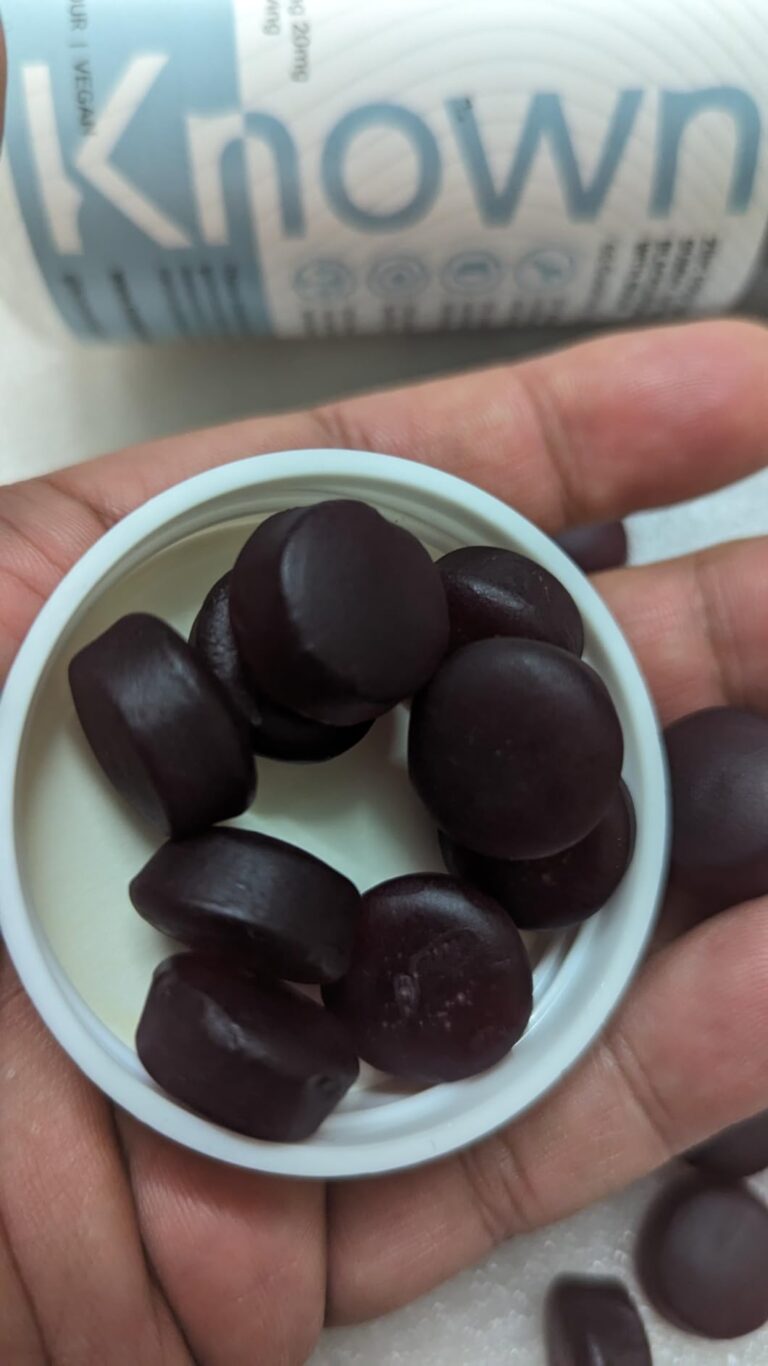 Gros plan sur une main tenant le couvercle de la bouteille de compléments alimentaires, rempli de gommes de zinc, sur fond bl...