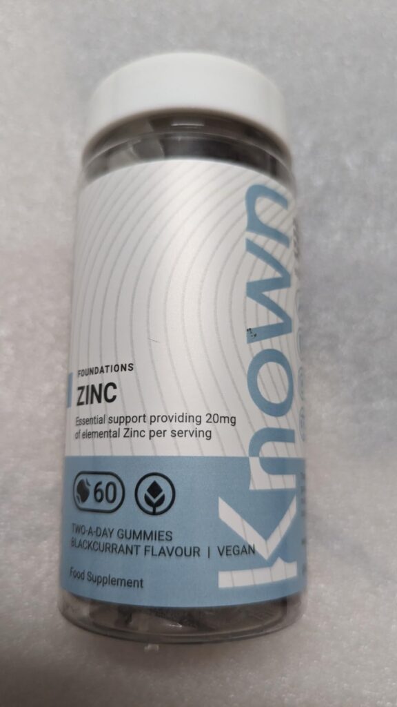 Bouteille de compléments alimentaires 'KNOWN ZINC', contenant 60 gommes, sur fond blanc. Texte visible sur l'étiquette : 'FOU...