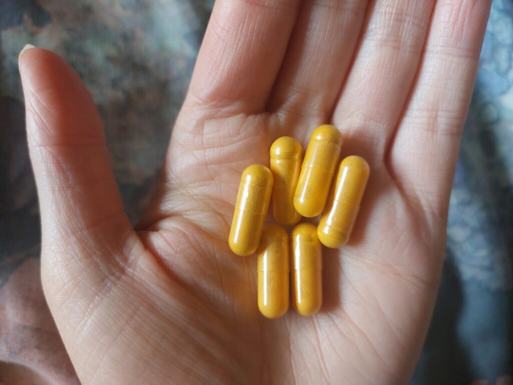 Une main ouverte avec 6 gélules de curcuma. Les gélules sont de couleur jaune.