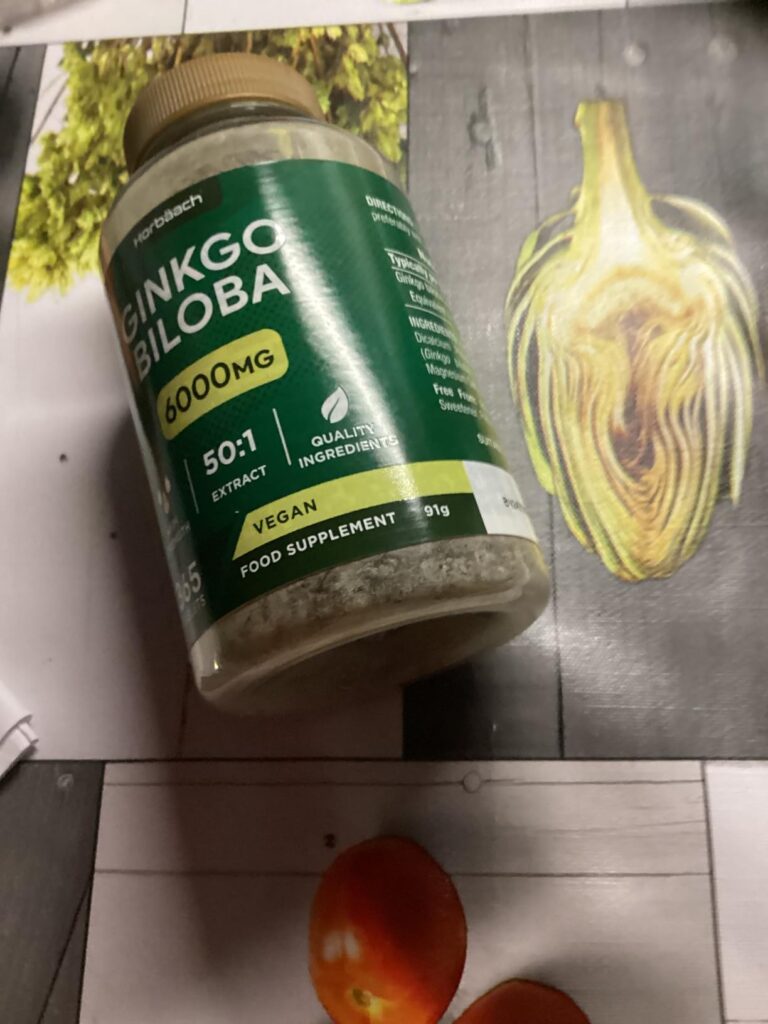 Le flacon de Ginkgo Biloba sur une table avec une demi-artichaut et des tomates cerises.