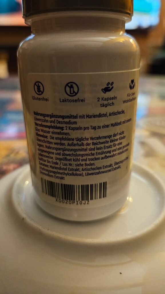 Dos du flacon de compléments alimentaires Mariendistel Komplex de la marque Gloryfeel, posé sur une assiette. On peut lire la...