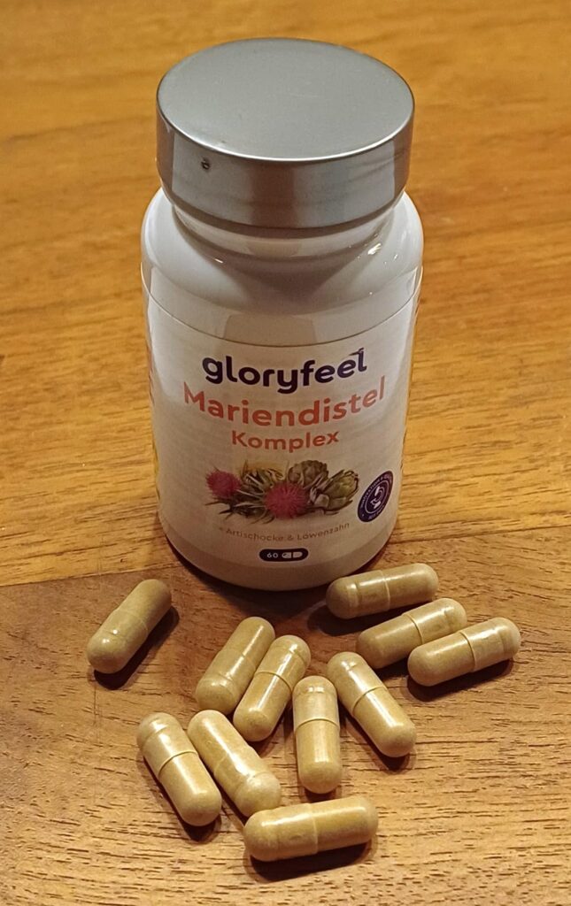 Flacon de compléments alimentaires Mariendistel Komplex de la marque Gloryfeel, posé sur une table en bois, avec plusieurs gé...