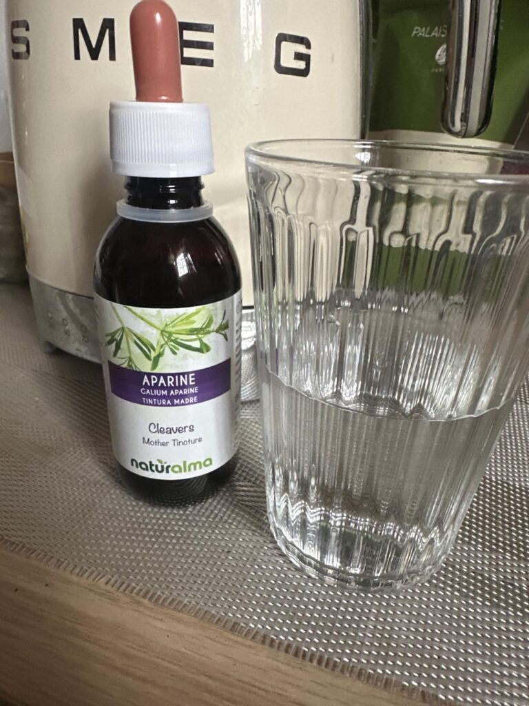 Flacon de teinture mère d'Apparine à côté d'un verre d'eau, sur un comptoir de cuisine.