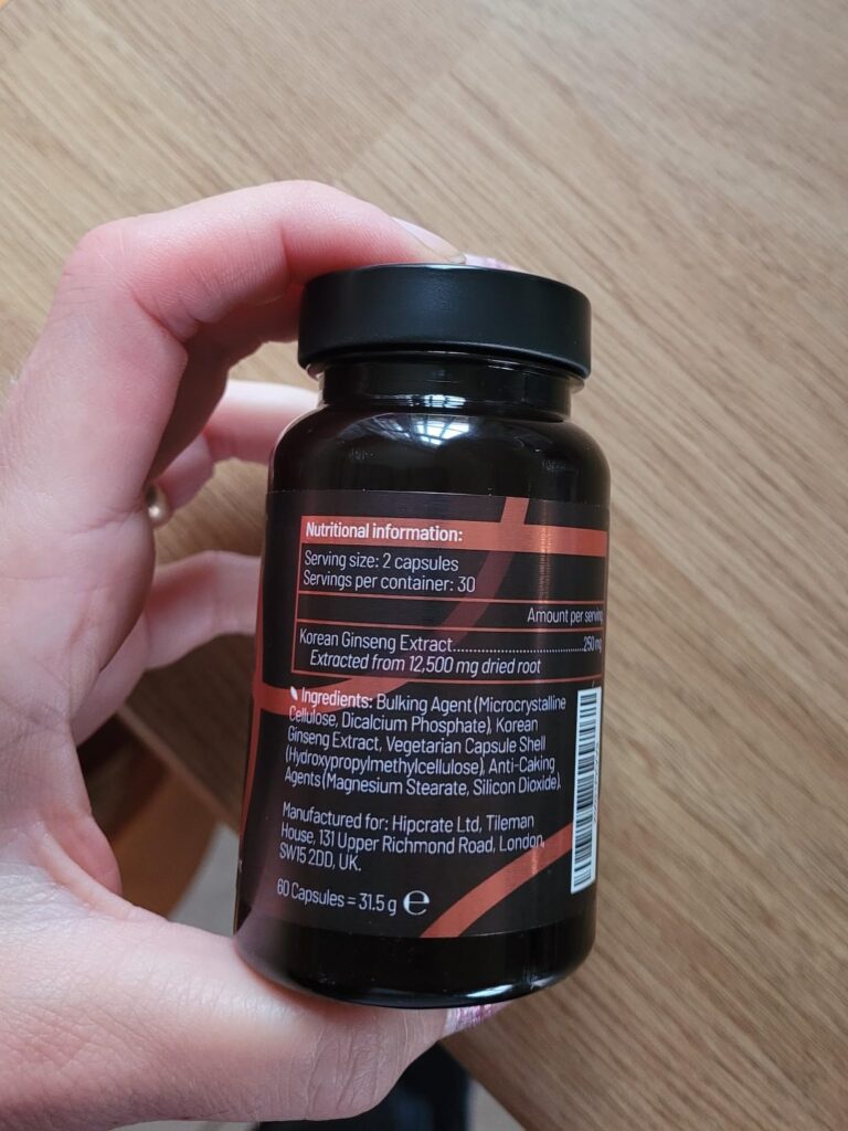 Bouteille de ginseng coréen Panax, tenue dans une main, vue de dos, sur un fond de plancher en bois. L'étiquette au dos est l...