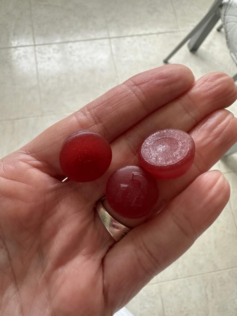 Trois gummies rouges dans une main, un d'entre eux est sectionné en deux.