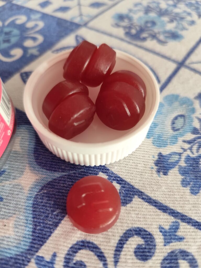 Plusieurs gummies rouges dans le bouchon du pot et un à côté, sur une table à carreaux bleus et blancs.