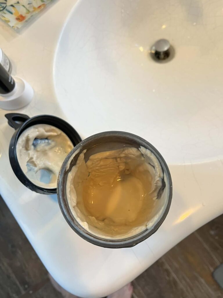 Le pot de protéines végétales ouvert avec le contenu mélangé, posé sur un lavabo, à côté d'un robinet.