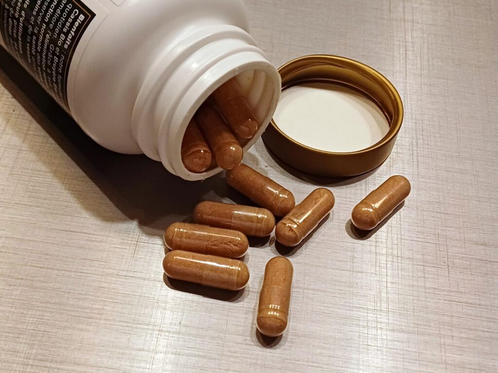 Plusieurs gélules de couleur marron-orangé sont visibles, certaines sortant du flacon renversé, d'autres éparpillées à côté d...
