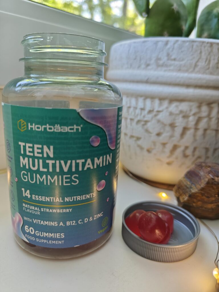Un pot de vitamines en gomme ouvert avec une gomme dans le couvercle, posé sur un rebord de fenêtre, avec une plante verte en...