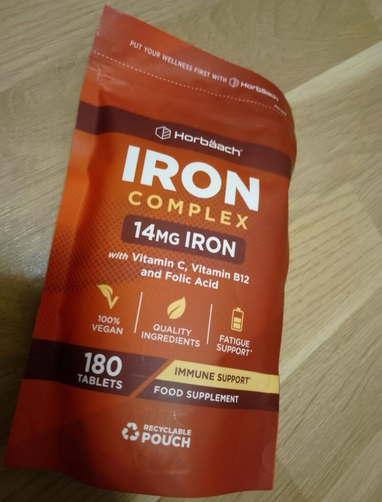 Un sachet de compléments alimentaires rouge sur fond clair, posé à plat et légèrement de biais.