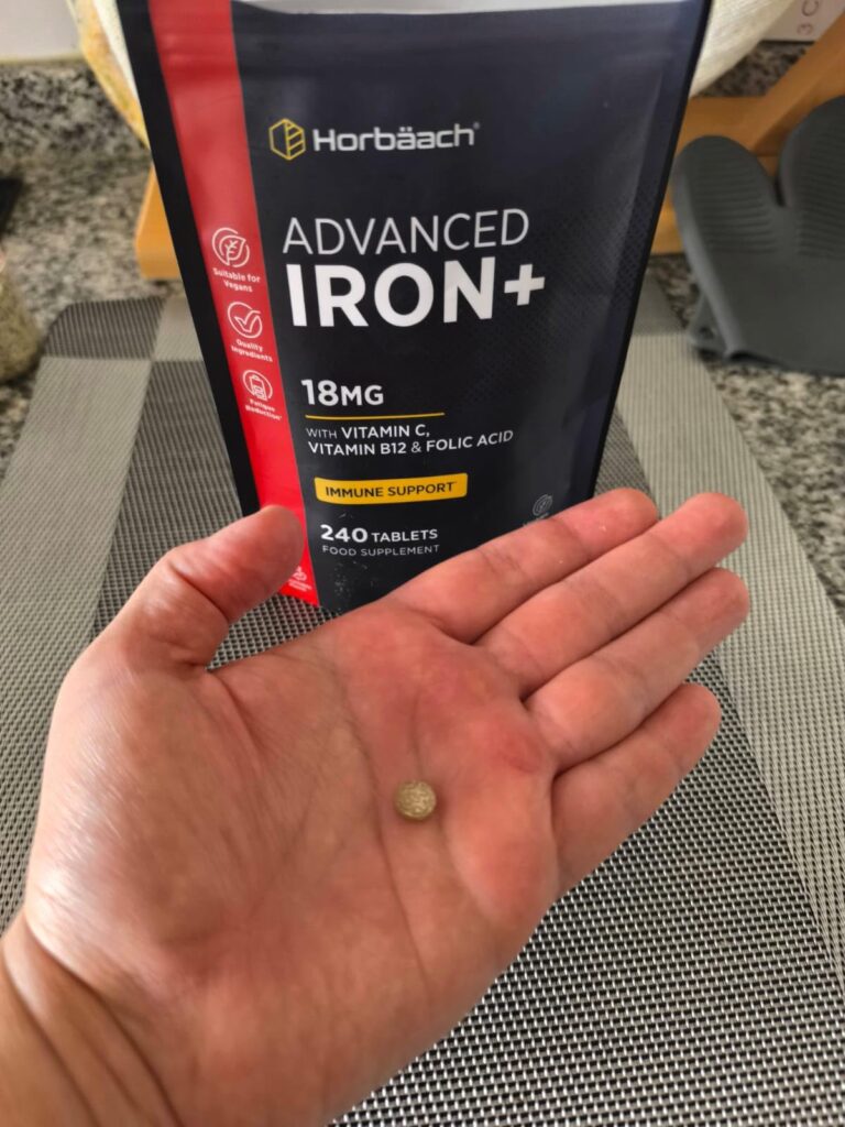 Un sachet de compléments alimentaires noir et un comprimé dans la main.
