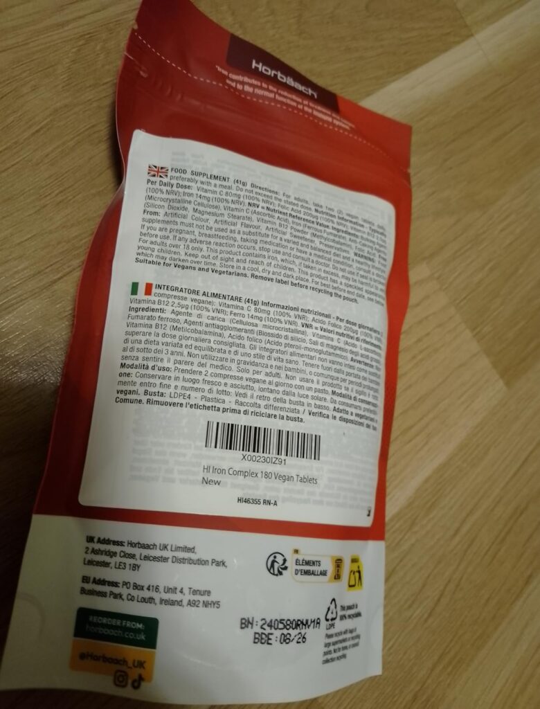 Le dos d'un sachet de compléments alimentaires rouge, posé à plat et légèrement de biais, montrant le code-barre et les infor...
