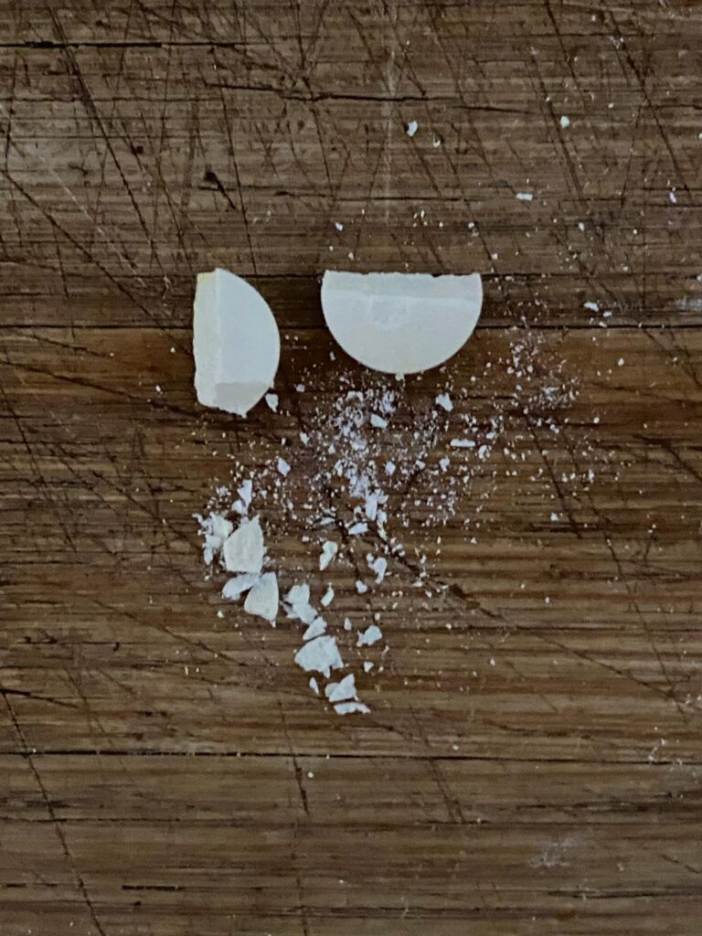 Vue de dessus d'une pastille cassée en deux, avec des petits morceaux éparpillés sur une planche en bois.