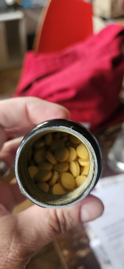 Vue de dessus du pot ouvert, montrant les comprimés jaunes à l'intérieur.