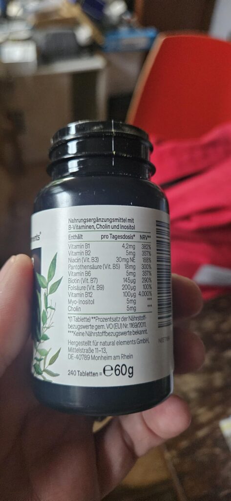 Le côté du pot de vitamines est tenu à la main, les informations nutritionnelles sont visibles.
