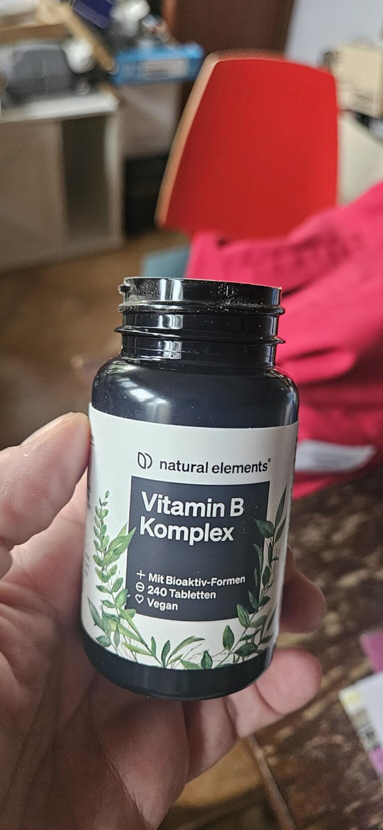 Le pot de vitamines est tenu à la main, l'étiquette est visible.