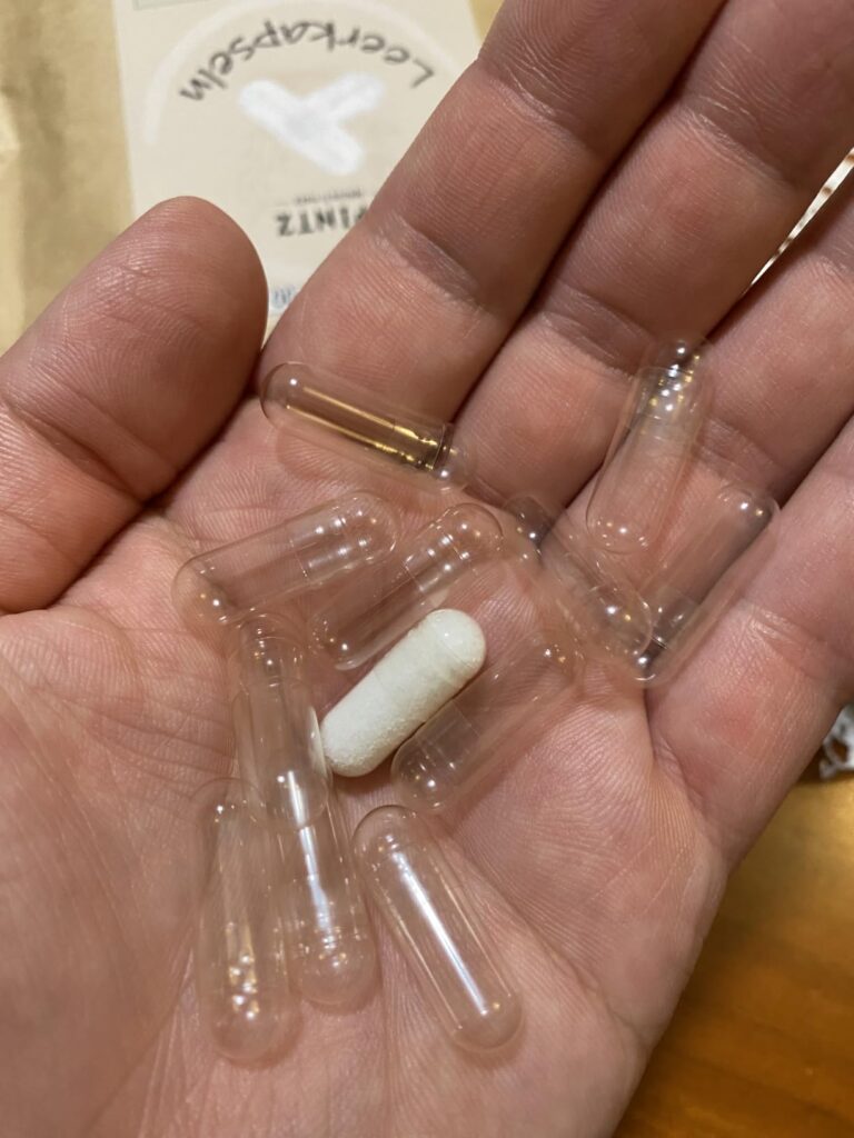 Une main ouverte contenant des capsules vides et une capsule remplie de poudre blanche.