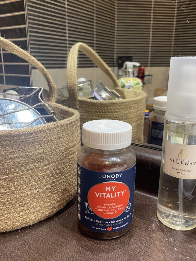 Bouteille de compléments alimentaires dans une salle de bain, avec des paniers de rangement et une bouteille de spray en arri...