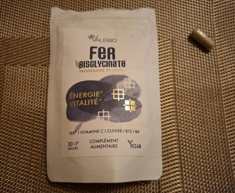 Le sachet du produit et une gélule posés sur une surface tressée foncée.
