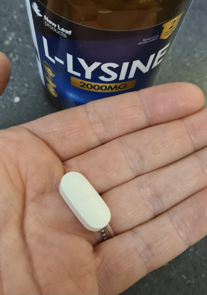 Une pilule de L-Lysine tenue dans une main, avec le flacon en arrière-plan.