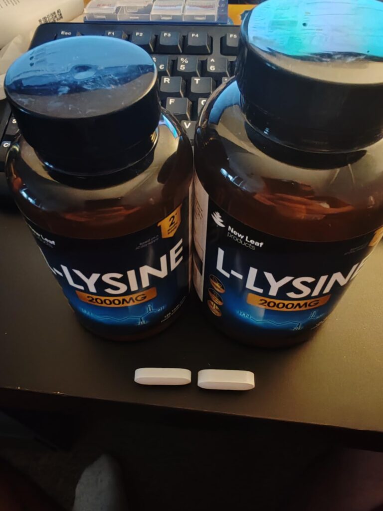 Deux flacons de L-Lysine et deux pilules posées devant eux sur un clavier d'ordinateur.