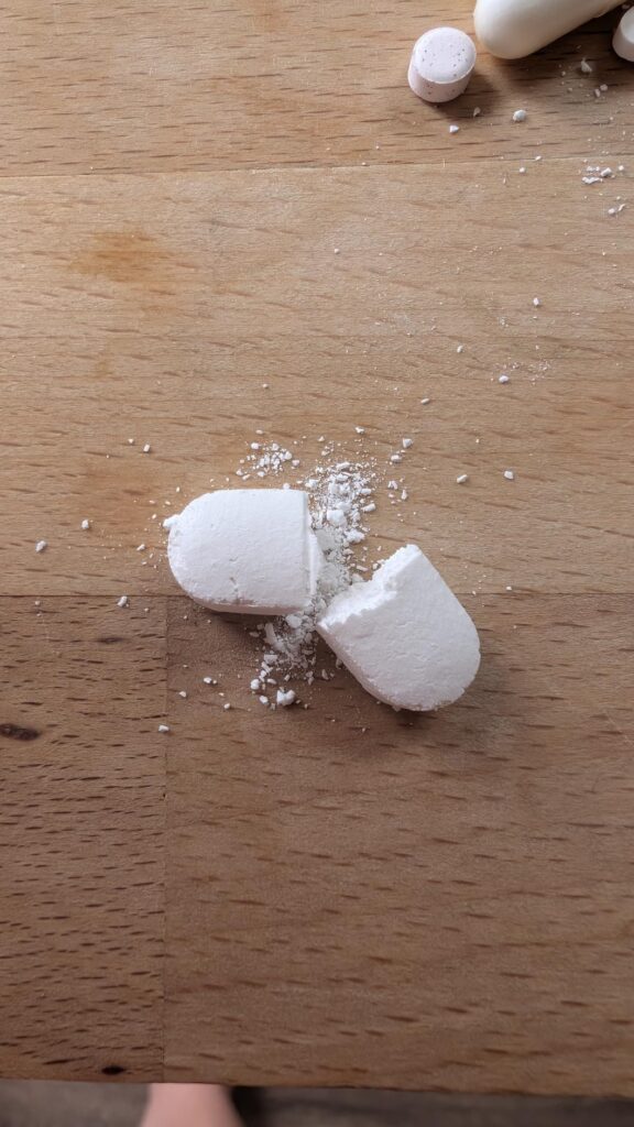 Une pilule de L-Lysine cassée en deux sur une planche en bois, montrant sa texture intérieure.