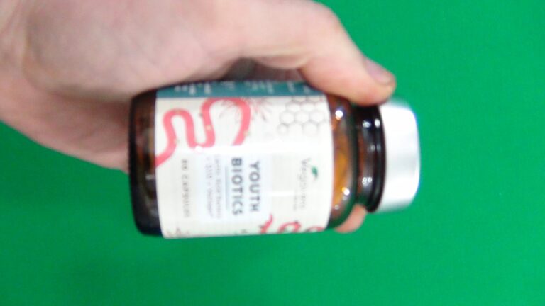 Main tenant une bouteille de probiotiques sur fond vert, le côté de la bouteille est visible.