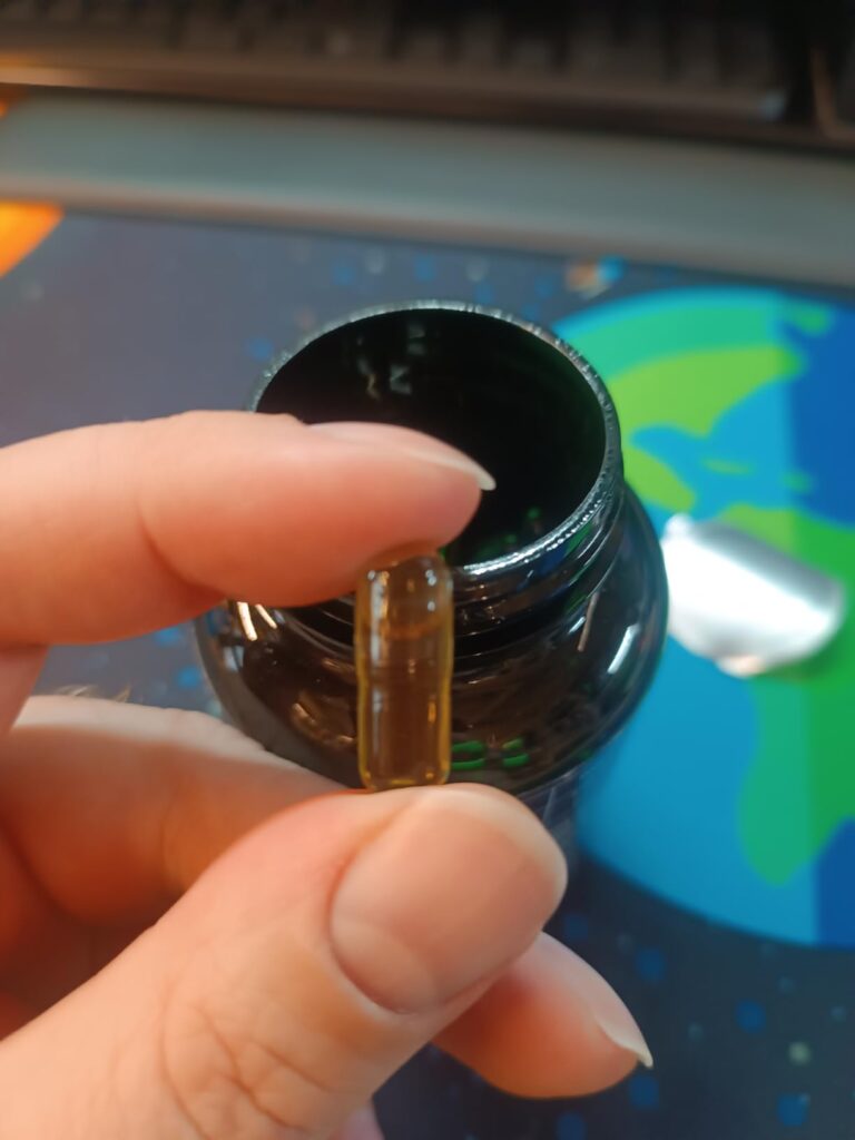 Main tenant une capsule d'huile d'onagre au-dessus du flacon ouvert.