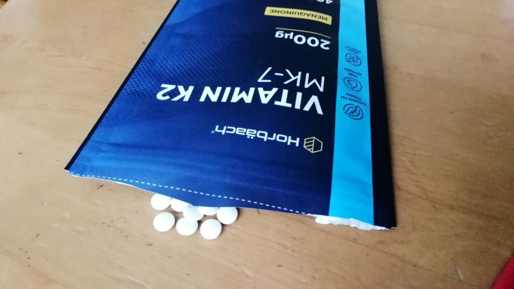 Sachet de vitamine K2 Horbäach ouvert avec des comprimés blancs qui en sortent.