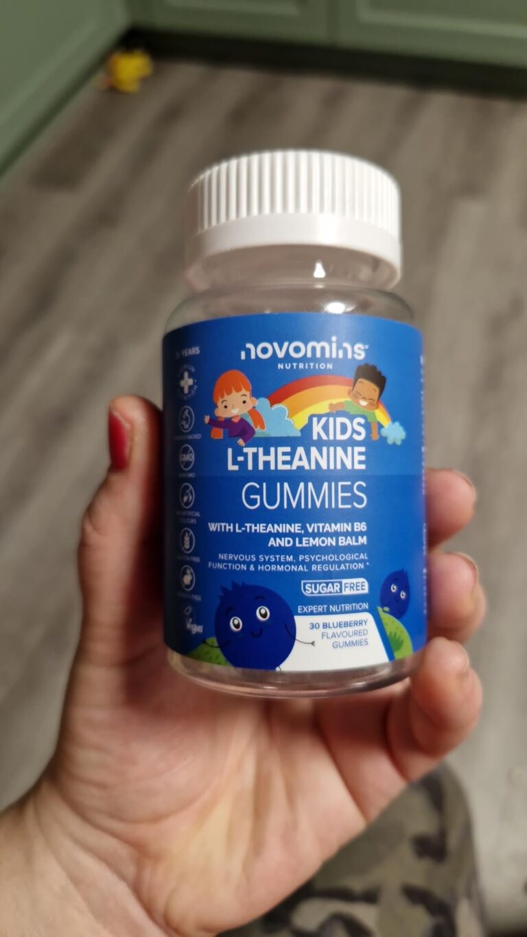 Flacon de compléments alimentaires pour enfants tenu dans une main, sur fond de cuisine.