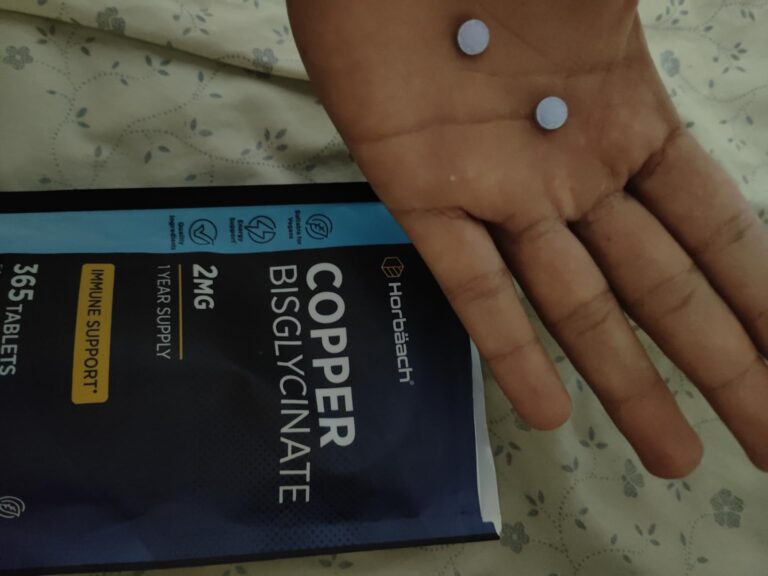 Deux comprimés de cuivre bisglycinate posés sur la paume d'une main, avec le paquet en arrière-plan.