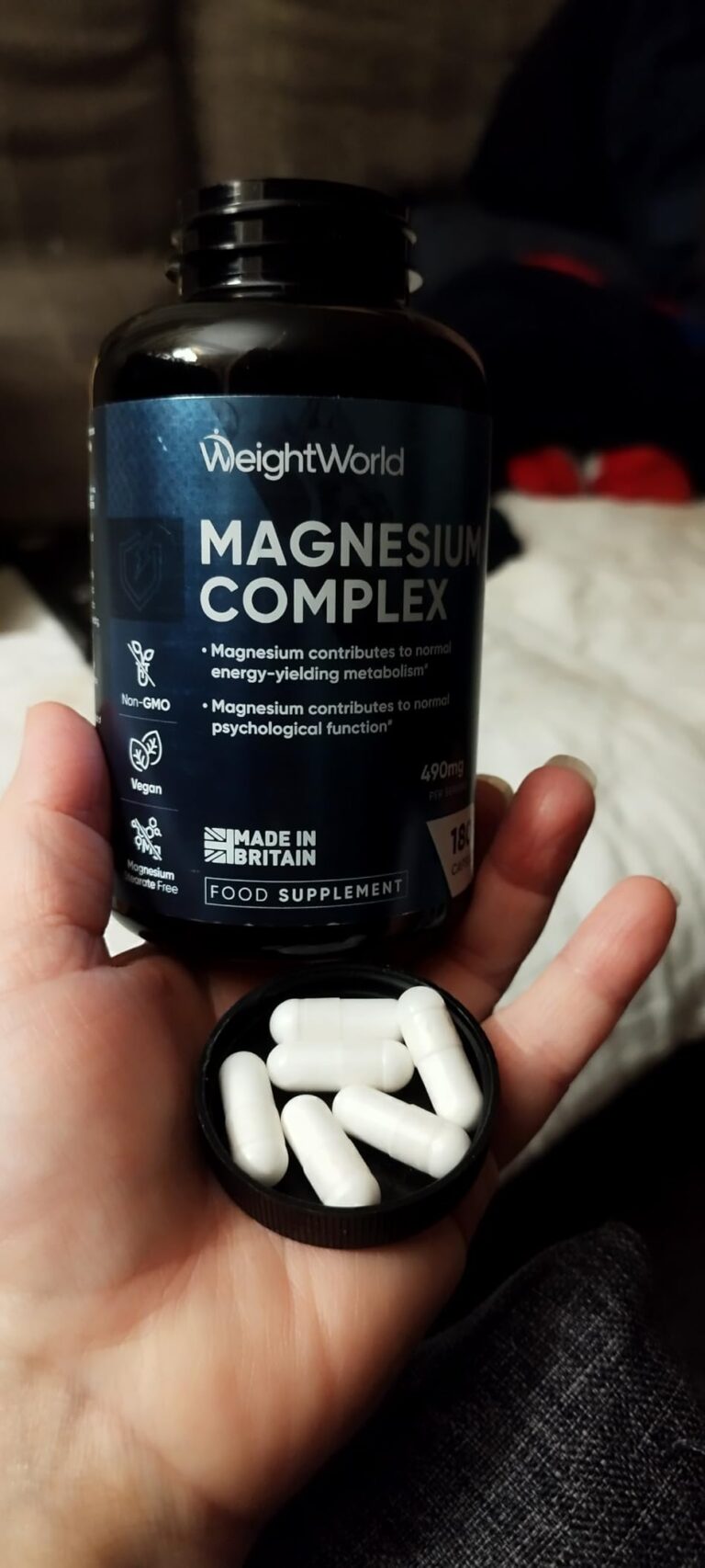 Main tenant la bouteille de compléments alimentaires Magnesium Complex de WeightWorld, avec quelques capsules dans le bouchon...