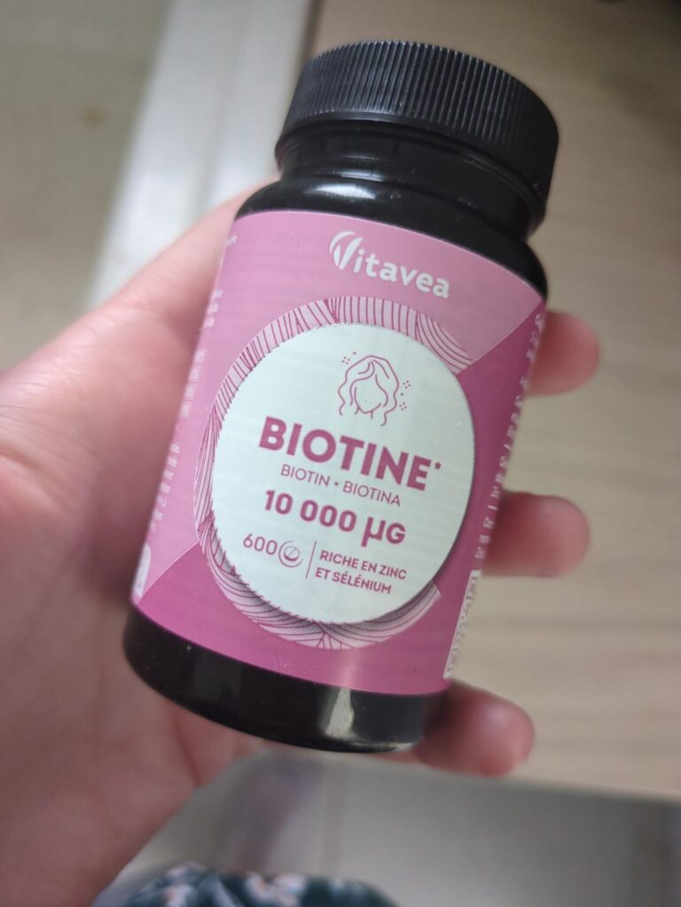 Une main tenant la même bouteille de Biotine que le visuel précédent, mais vue de face, sur un fond de salle de bain.