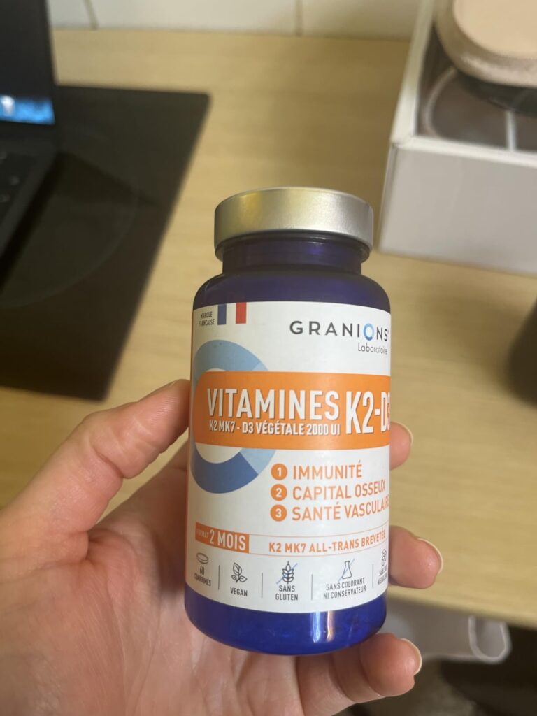Flacon de vitamines K2-D3 tenu dans une main, avec une étiquette en français
