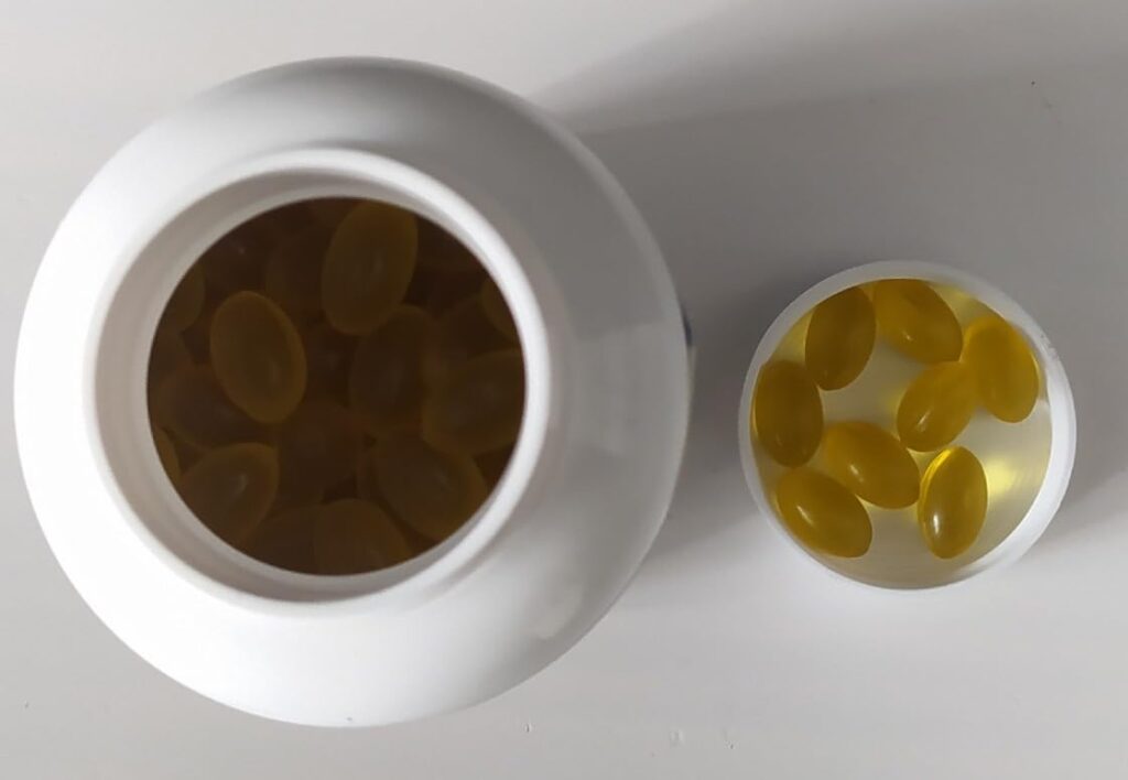 Flacon de compléments alimentaires, vue de dessus, avec le couvercle dévissé. On voit des capsules jaunes à l'intérieur du fl...