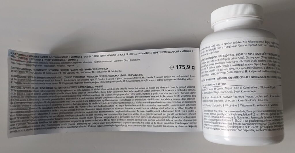 Flacon de compléments alimentaires posé sur le côté, avec l'étiquette décollée, montrant le texte légal et le poids net du pr...