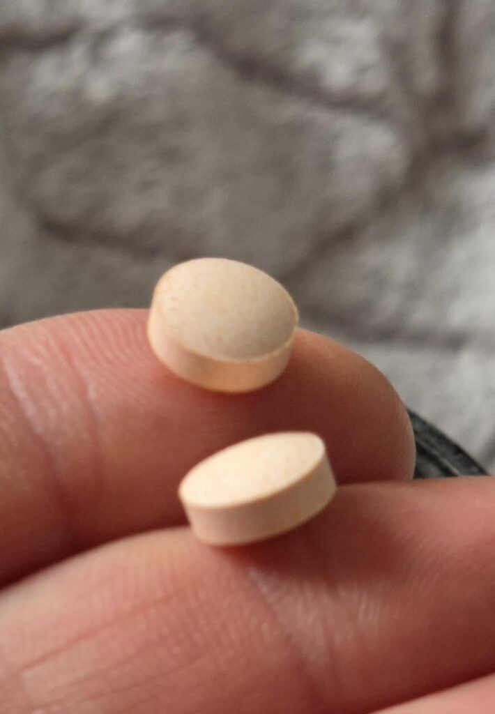 Gros plan sur deux comprimés ronds et beiges, posés sur un doigt.