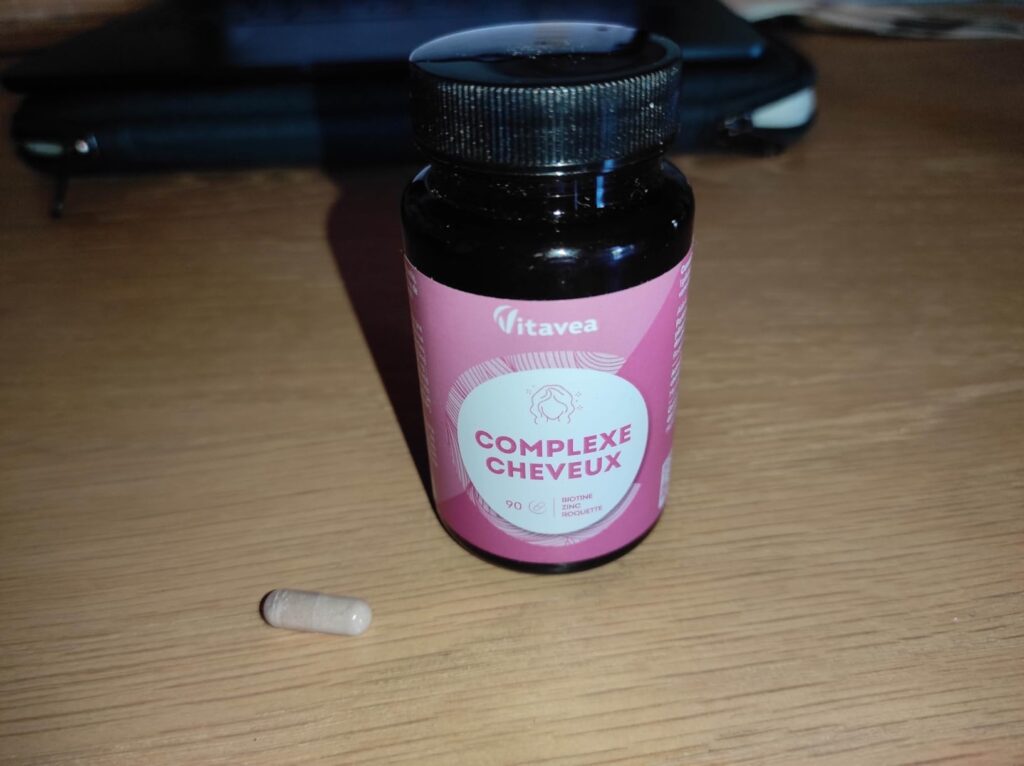 Bouteille du produit sur une table avec une gélule. Montre le même produit que les images 0 et 2.