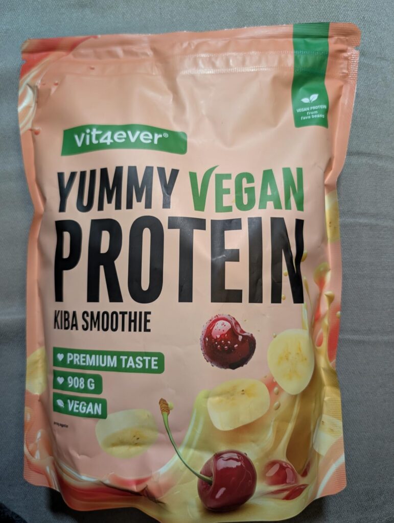 Vue d'ensemble du sachet de protéines vegan Vit4ever Yummy Vegan Protein Kiba Smoothie sur un fond uni et sombre. Le sachet e...