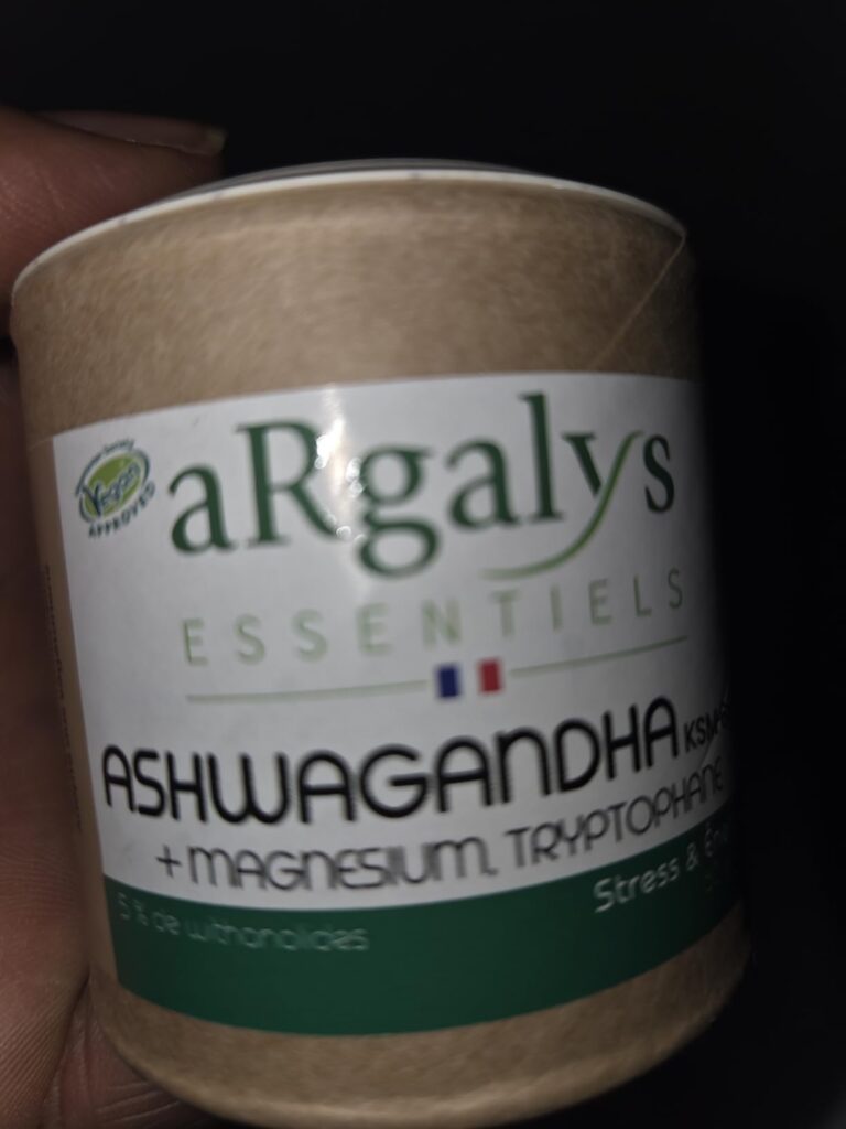 Vue frontale du pot de compléments alimentaires Ashwagandha, légèrement incliné. Le pot est en carton kraft et l'étiquette bl...