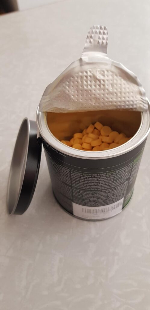 Vue en gros plan sur le pot de compléments alimentaires ouvert, on voit les petits comprimés à l'intérieur.