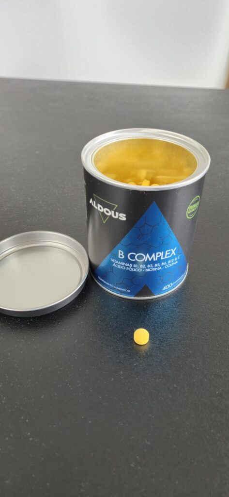 Le pot de compléments alimentaires ouvert avec le couvercle à côté et un comprimé posé sur la table.