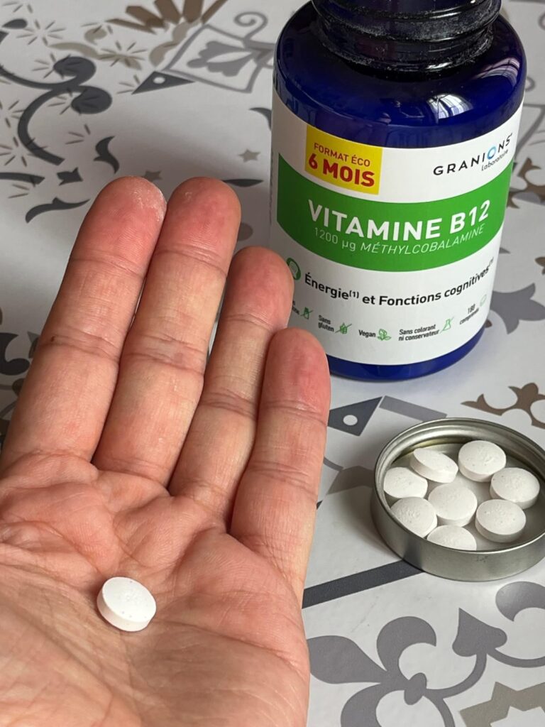 Un comprimé de vitamine B12 dans la main, plusieurs comprimés dans le bouchon de la bouteille, et la bouteille derrière, sur...